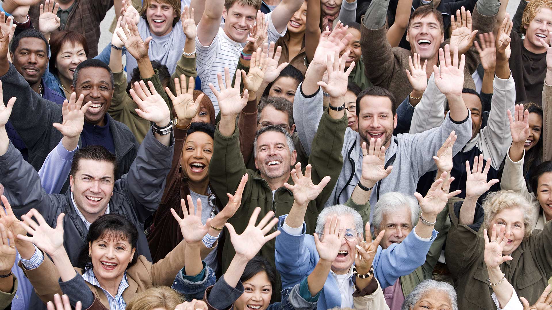 Photo of crowd of diverse people with their hands in the air.